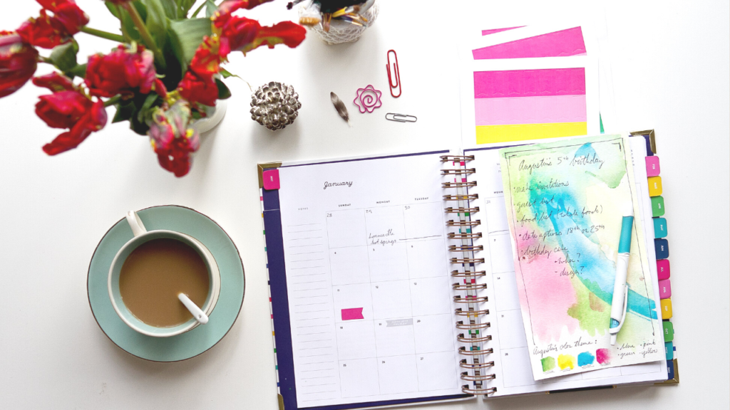 planner with colorful tabs on a table with a cup of tea and flowers