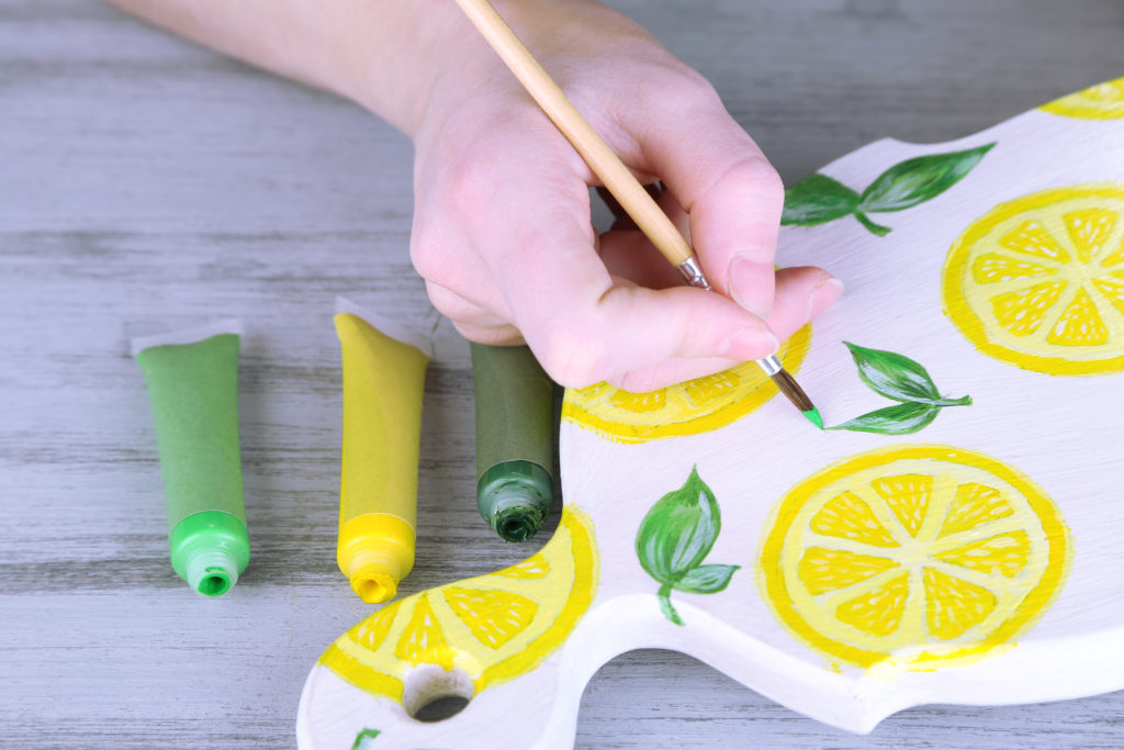 a hand painting a wooden board with a lemon and leaf design