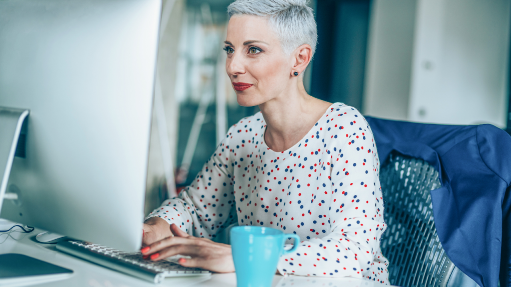 A woman smiling at her computer screen while sitting at her desk working on email marketing best practices