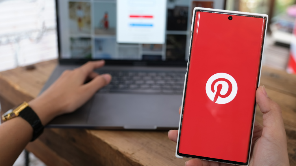 Pinterest loading on a cell phone with a laptop in the background.